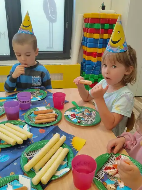Przedszkolaki w urodzinowych czapeczkach przy stole