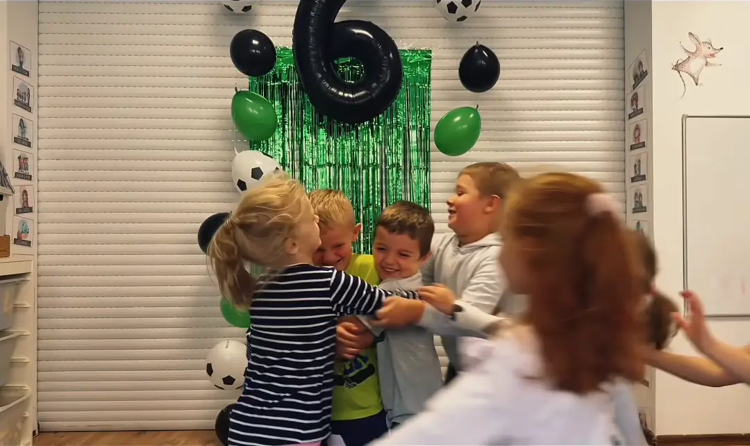 Przedszkolaki tańczą przed urodzinową dekoracją z piłkarskimi balonami